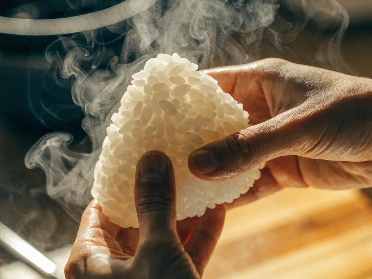 Mains façonnant un onigiri avec du riz vapeur fumant