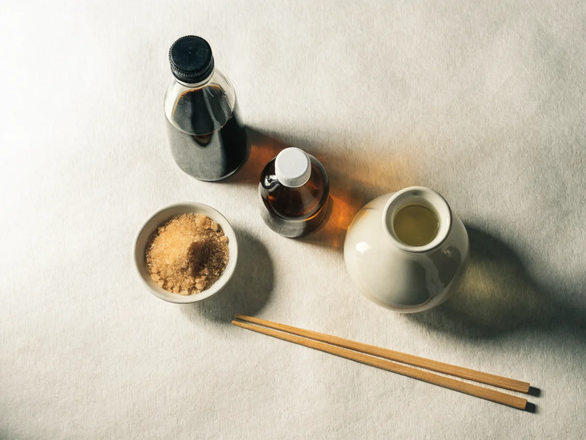 Les 4 ingrédients de la sauce teriyaki maison : shoyu, mirin, saké et sucre roux, présentés sur fond washi