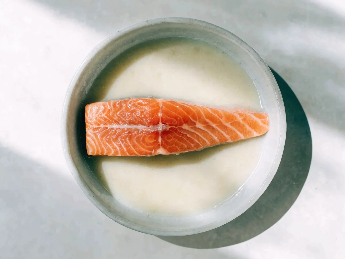 Filet de saumon cru posé à plat dans une marinade de miso blanc clair