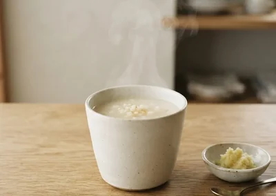 Bol d'amazake blanc et crémeux, quelques grains de koji de riz posés à côté, sur fond de papier washi